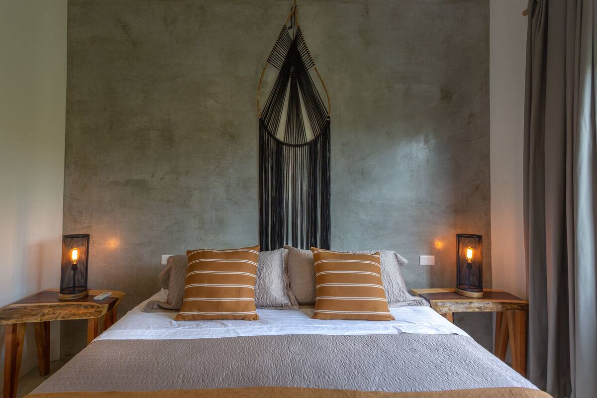 A bed with two pillows, a textured blanket, and a wall hanging. There are two bedside tables with lamps.