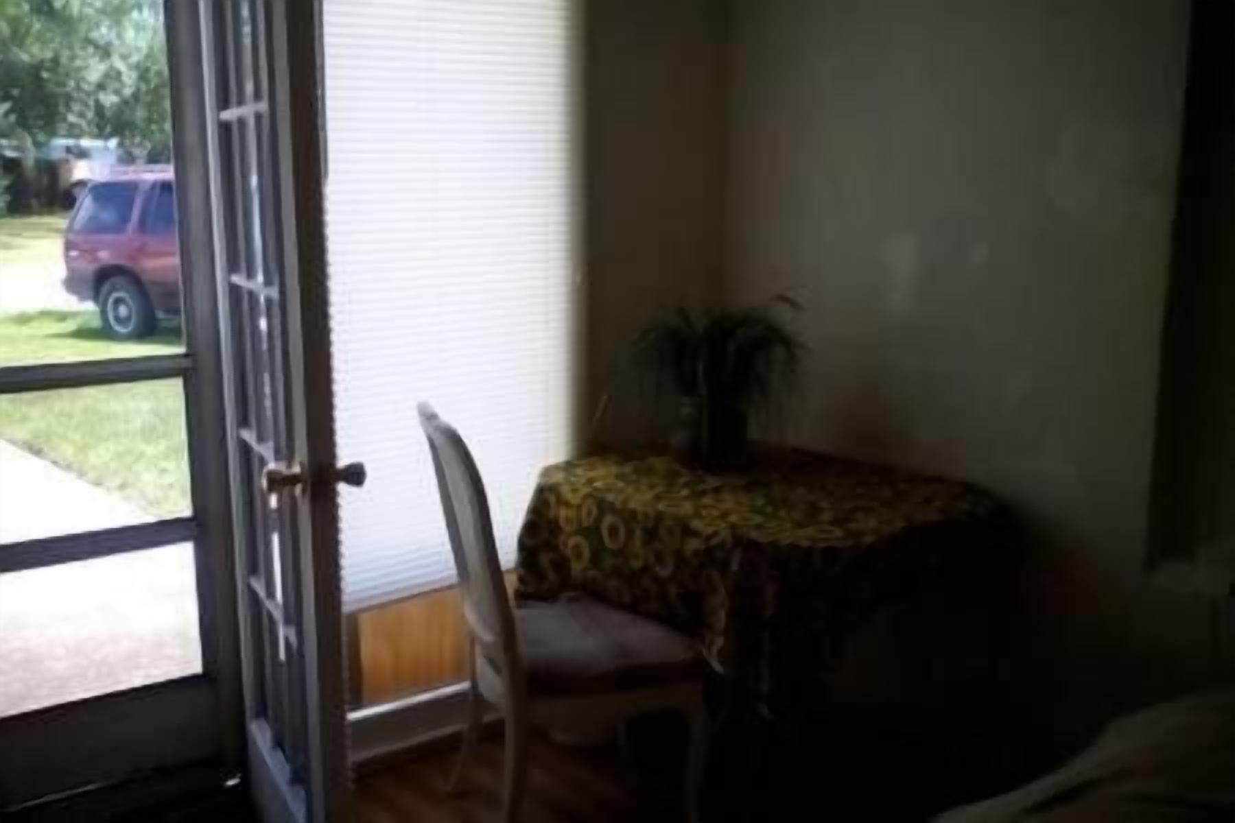 A room with a chair, a table with a patterned tablecloth, and a window with a view of a parked car outside.