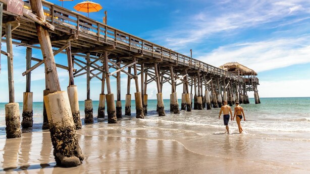 Un muelle de madera que se adentra en el mar, con dos sombrillas.
