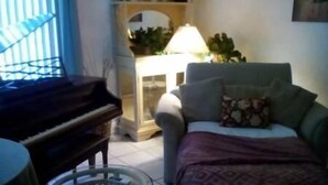 Una sala de estar con un piano, un sofá, una lámpara y un plaid estampado.