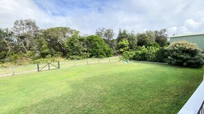 A grassy outdoor area with a fence, trees, and a building in the background. - 54 Kendall - Surrounded by Yuragrir National Park (WOOLI)
