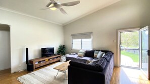 Un salon équipé d’un téléviseur à écran plat, d’un meuble de rangement en bois, d’un canapé noir, d’une table basse et d’un ventilateur de plafond.
