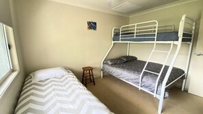 Une chambre avec deux lits superposés, un petit tabouret et un lit simple recouvert d’une courtepointe à motifs chevrons.