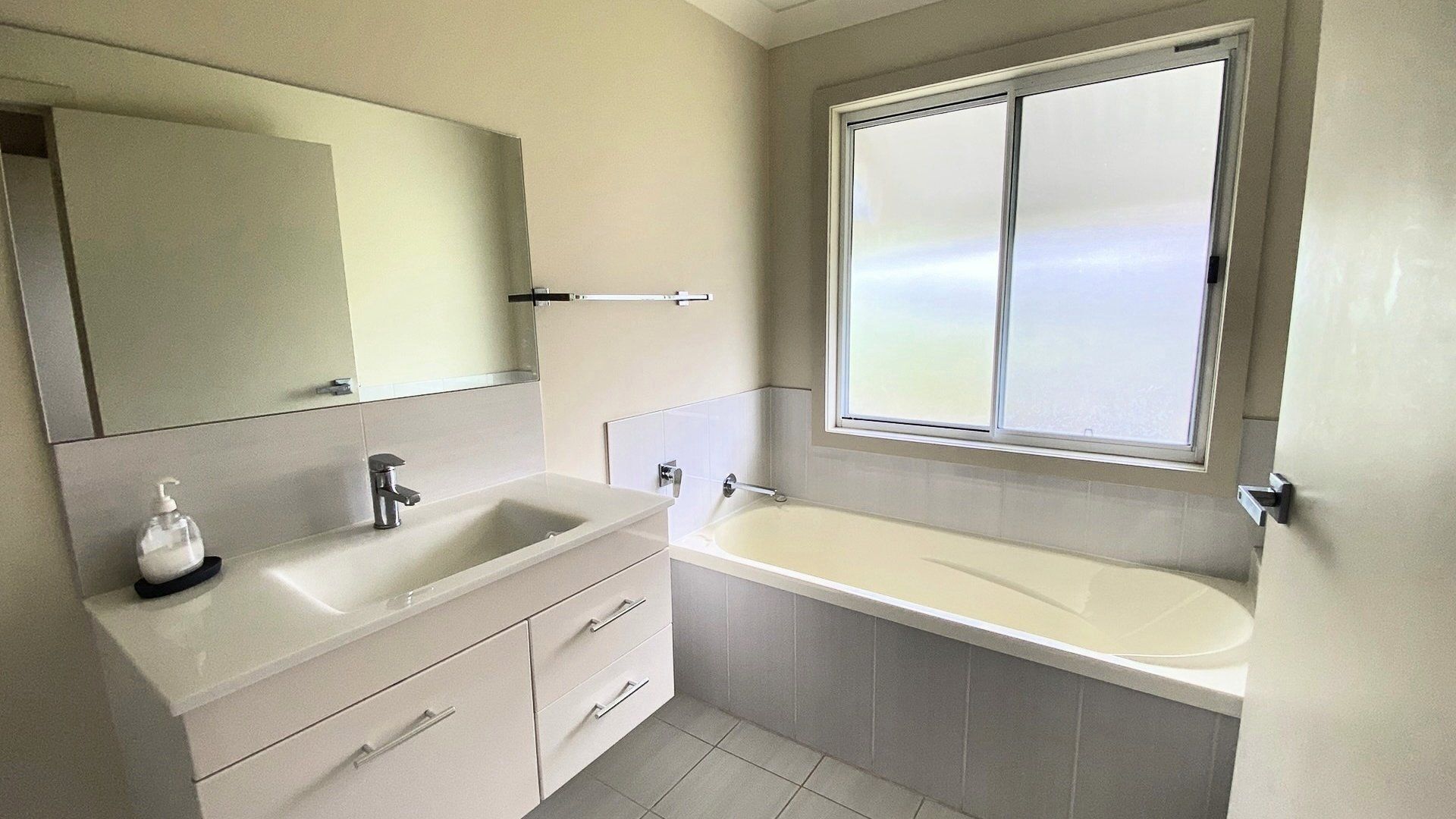A modern bathroom with a large mirror, a sink, a bathtub, and a window.
