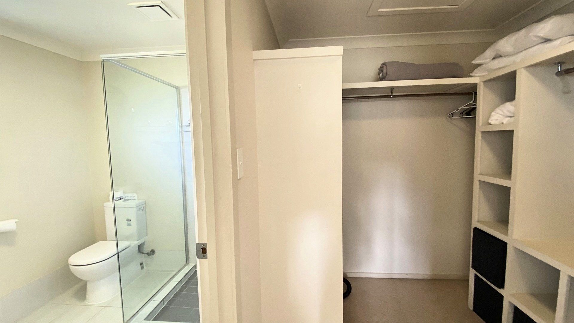 A bathroom with a toilet, a glass shower enclosure, and a walk-in closet with shelves and hanging space.