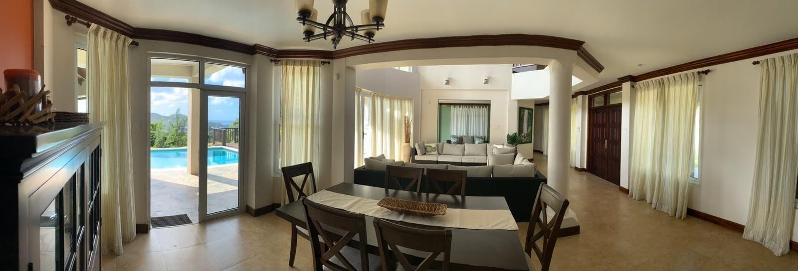 Ampla sala de estar com mesa de jantar, sofás e vista para uma piscina.