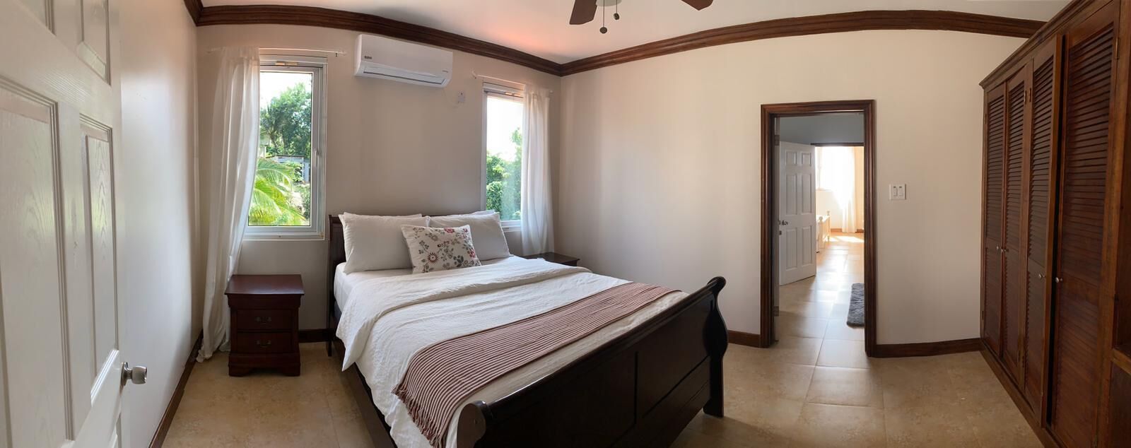 Quarto com cama, mesa de cabeceira, guarda-roupa e janela com cortinas.
