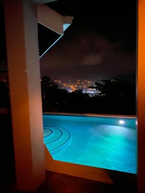 A nighttime view from a balcony with a swimming pool, overlooking a cityscape with illuminated buildings. - Villa Xona (Castries)
