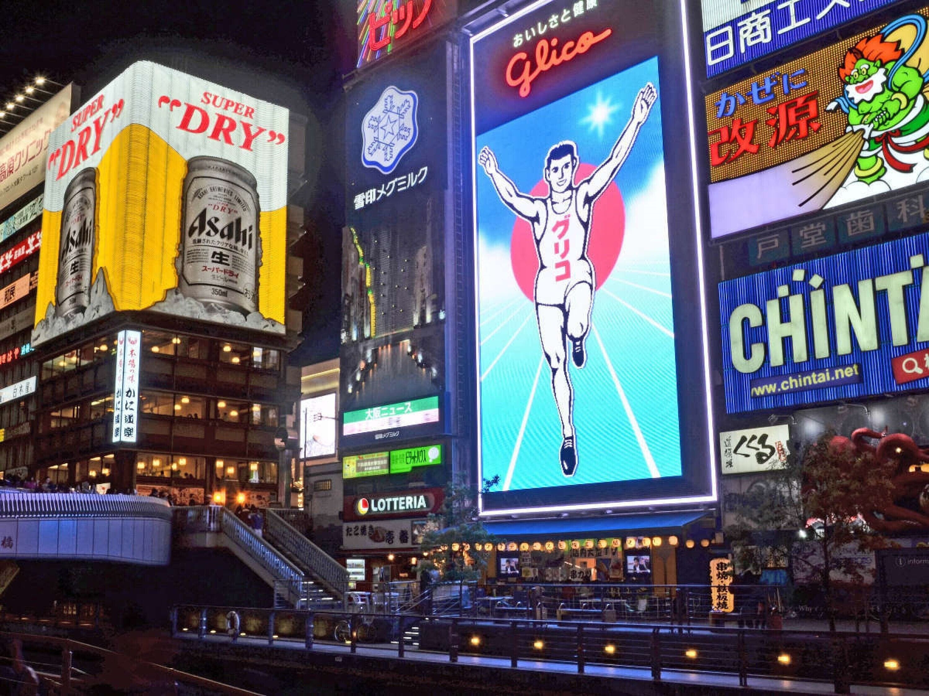 A busy urban street at night with illuminated billboards and signage.