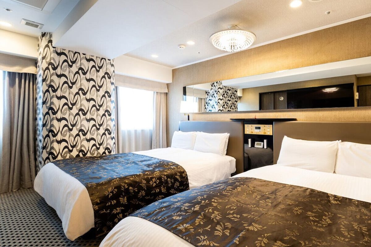 A hotel room with two beds, a large mirror, a flat-screen TV, and a desk with a lamp.