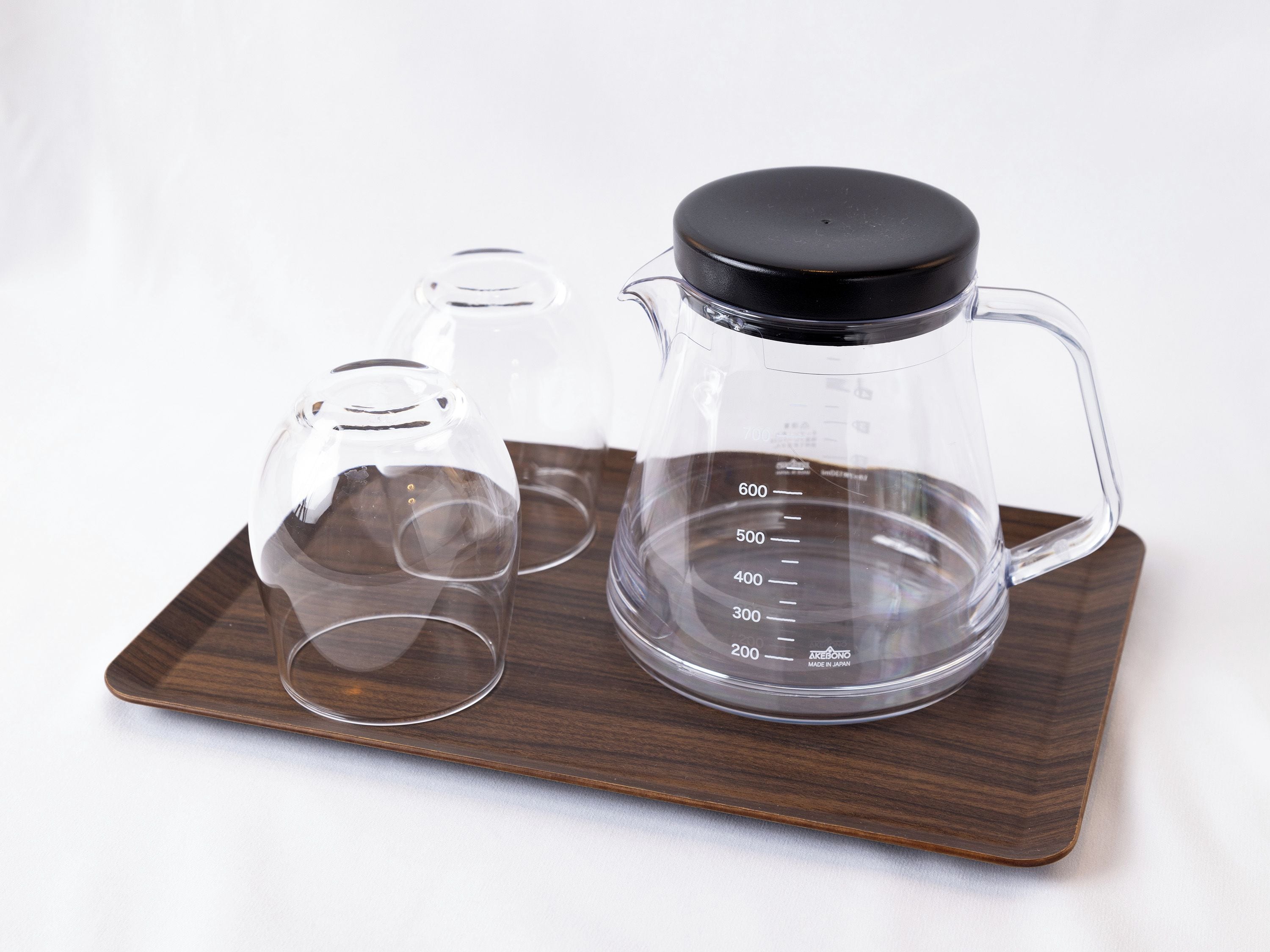 A coffee maker with a measuring cup and two glasses on a wooden tray.