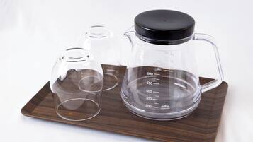 A coffee maker with a measuring cup and two glasses on a wooden tray.