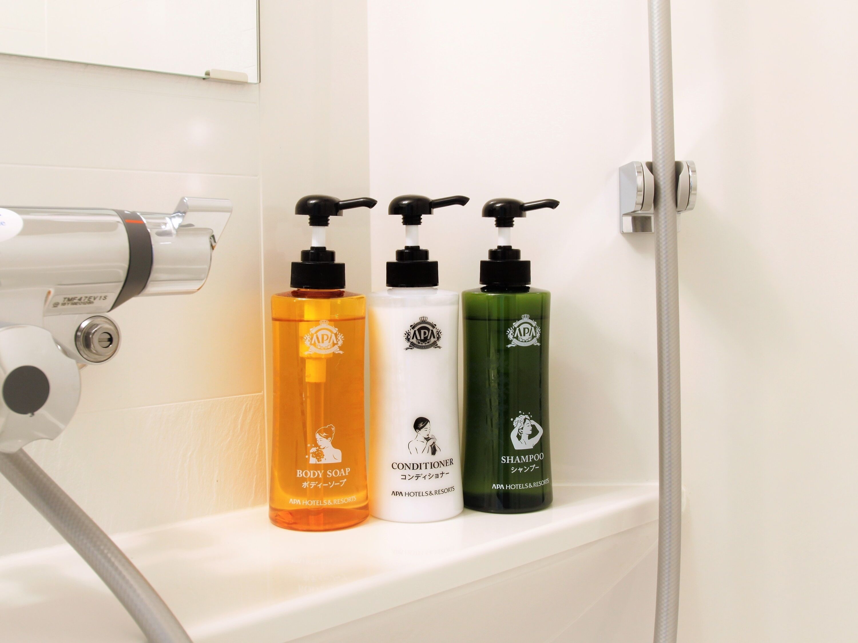 Une étagère de salle de bain contenant trois bouteilles de savon pour le corps, d’après-shampoing et de shampoing, chacune portant le logo d’APA Hotels & Resorts.