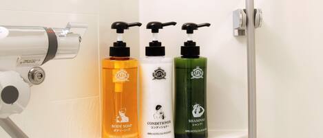 Une étagère de salle de bain contenant trois bouteilles de savon pour le corps, d’après-shampoing et de shampoing, chacune portant le logo d’APA Hotels & Resorts.