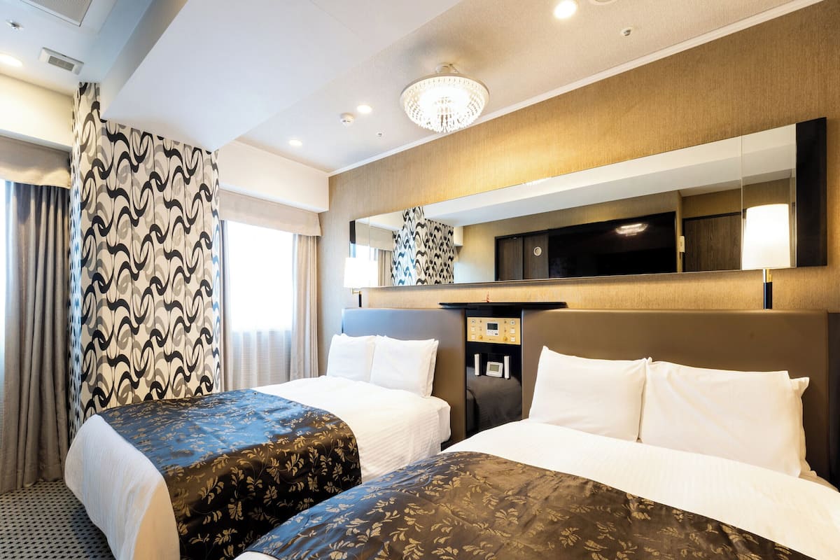 A hotel room with two beds, a minibar, a television, and a large mirror.