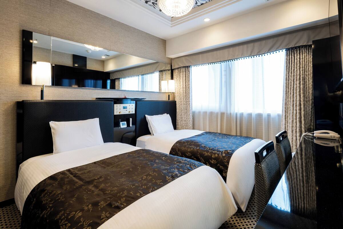 A hotel room with two beds, a large mirror, a desk with a telephone, and a television.