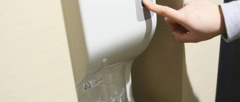 A hand pressing a button on a dispenser, likely for water or beverages.