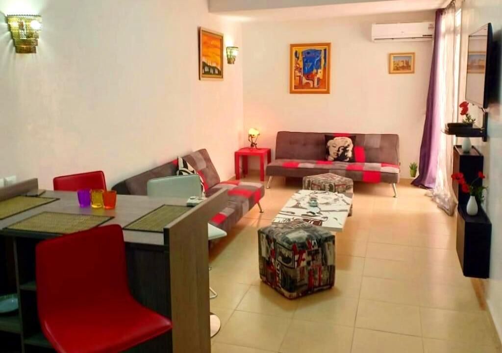 Un salon comprenant un canapé, un pouf, une table basse et un coin repas avec des chaises et une table.