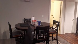 A dining area with a round table, six chairs, and a painting on the wall.