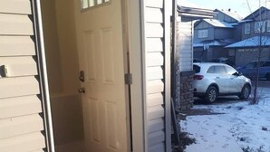 A garage door open with a car parked inside, a driveway with snow, and a house in the background.