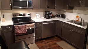 A modern kitchen with stainless steel appliances, dark cabinets, and a marble countertop.