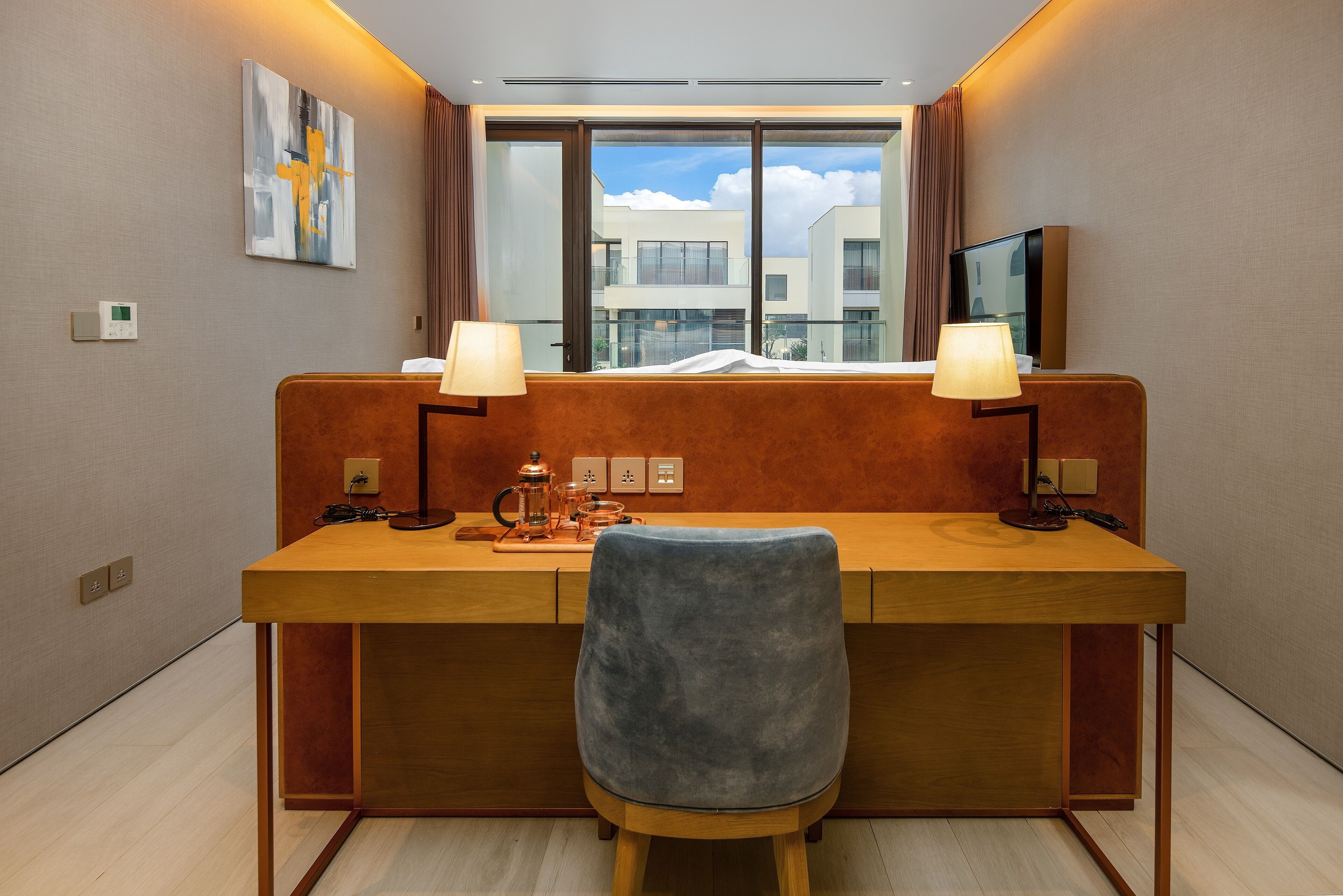 Une chambre d’hôtel avec un bureau en bois, deux lampes, une chaise, une fenêtre donnant sur des immeubles et un téléviseur à écran plat.