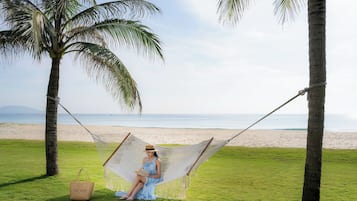 A hammock with a person sitting in it, a beach, and palm trees.