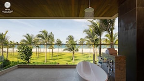 A modern bathroom with a large bathtub, a shower, and a view of a beach and palm trees. - The Five Villas & Resort Quangnam - Danang (Da Nang)