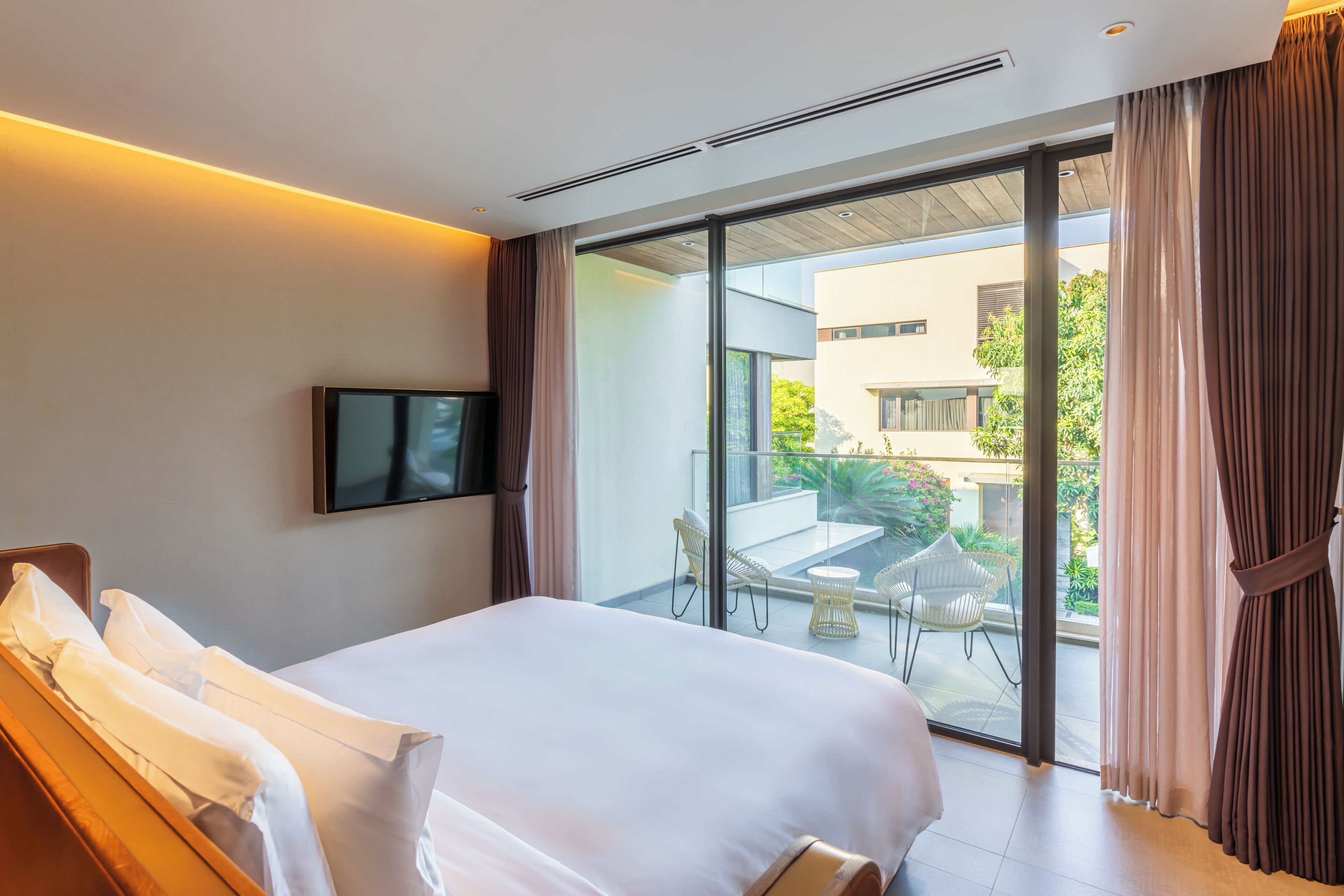 A hotel room with a large bed, a flat-screen TV, and a balcony with outdoor furniture.