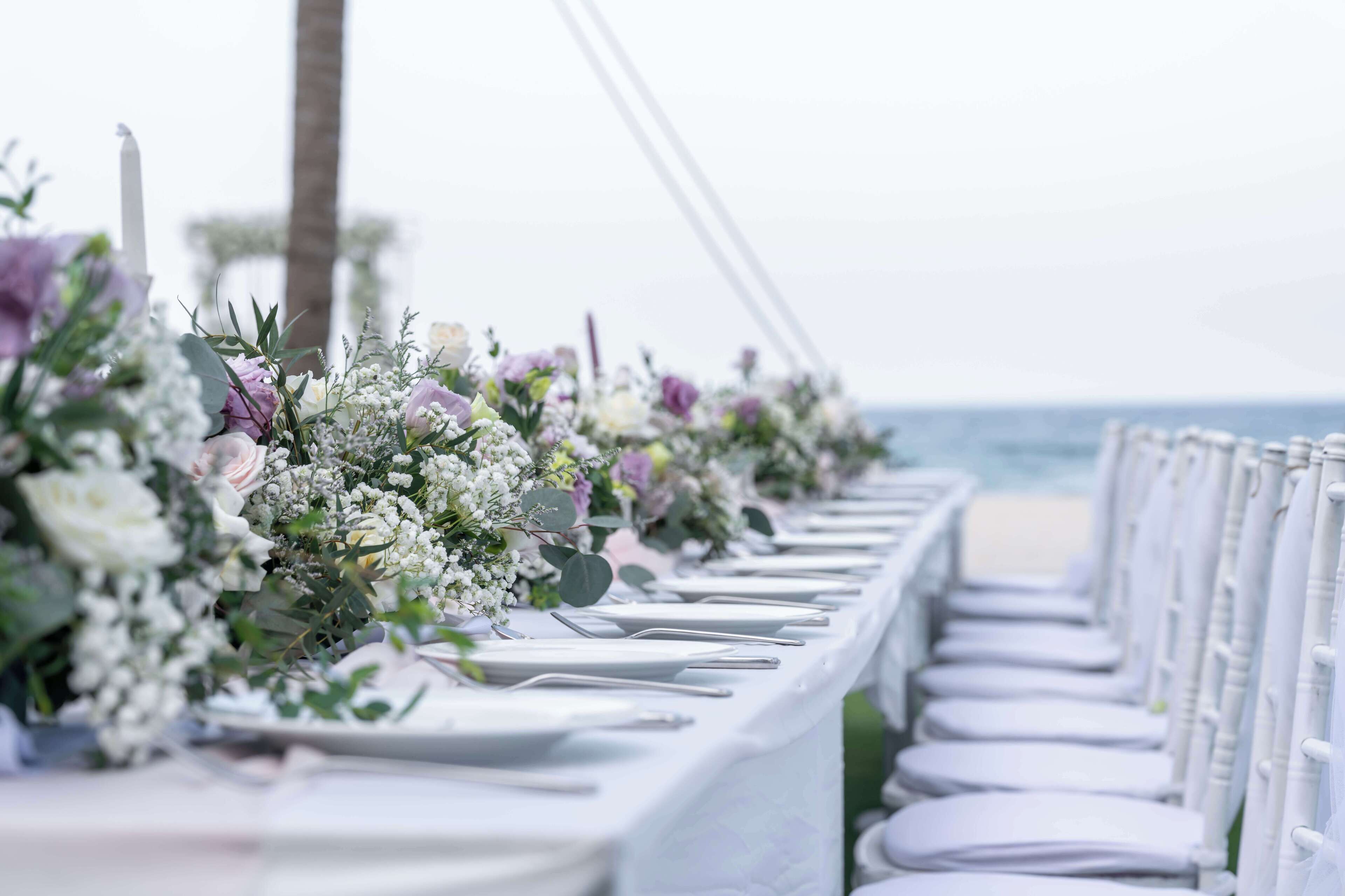 A long table with white tablecloths and chairs, decorated with floral arrangements.