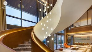 A modern interior with a curved staircase, a seating area with sofas, and a dining space. - The Five Villas & Resort Quangnam - Danang (Da Nang)