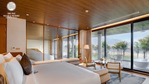 A modern hotel room with a large bed, seating area, and a view of palm trees. - The Five Villas & Resort Quangnam - Danang (Da Nang)