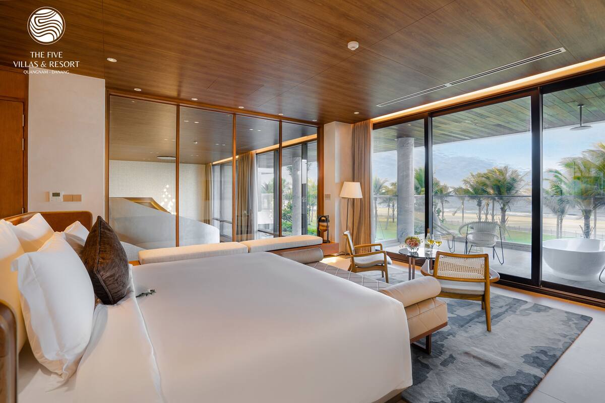 A modern hotel room with a large bed, seating area, and a view of palm trees.