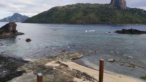 A coastal landscape with clear water, rocky shore, and a prominent mountain in the background. - Ocean view garden homestay (Wayasewa)