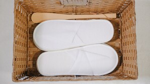 A wicker basket containing two white slippers and a wooden spoon. - Allcomein Hotel (Tokyo)