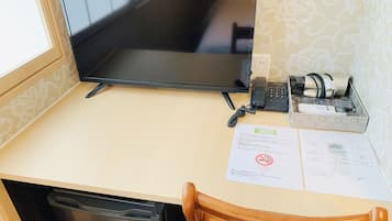 Une chambre d’hôtel équipée d’un grand téléviseur à écran plat, d’un téléphone, d’un appareil photo et d’un petit bureau avec des documents.