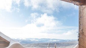 A room with a large window overlooking a snowy landscape and a hot tub area. - True Ski in/Ski out Hot tub In the village (Big White)
