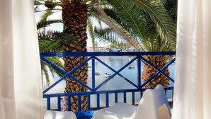 A balcony with a blue railing, palm trees, and a view of boats on the water.
