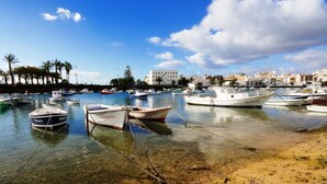 A marina with several boats docked, clear shallow water, and a sandy beach.