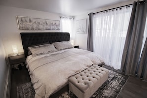 Un dormitorio con una cama grande, una mesita de noche con lámpara y una ventana con cortinas.