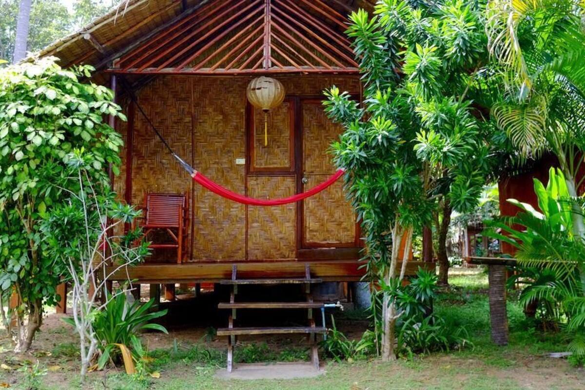 Une cabane en bois, coiffée d’un toit de chaume, entourée d’une végétation luxuriante.