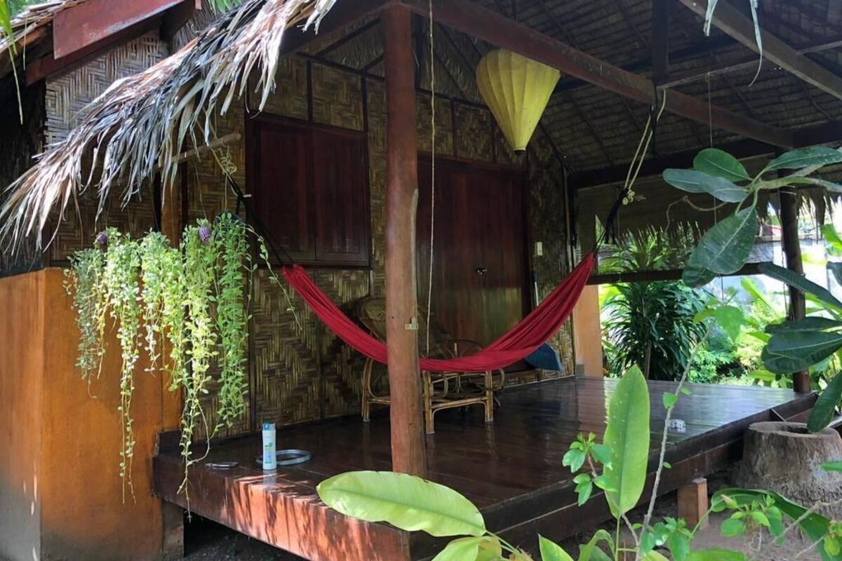 Une structure en bois avec un toit de chaume, un hamac et un petit espace piscine.
