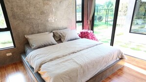 A modern bedroom with a large bed, a concrete wall, and a view of the outdoors.