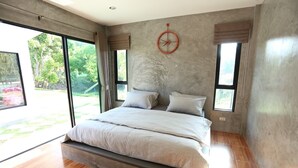 A modern bedroom with a large bed, a wall clock, and large windows offering a view of the outdoors.