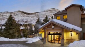 A hotel entrance with a snow-covered roof, a visible clock, and a mountainous backdrop. - Streamside at Vail Birch (Vail)