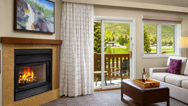 A living room with a fireplace, a sofa, a coffee table, and a view of a garden through a sliding glass door. - Streamside at Vail Birch (Vail)