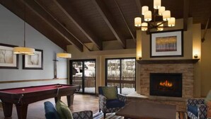 A cozy living room with a pool table, comfortable seating, a fireplace, and large windows. - Streamside at Vail Birch (Vail)