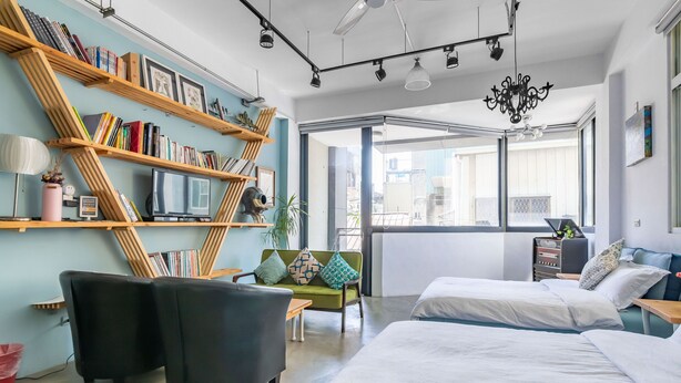 Ein modernes Hotelzimmer mit einer großen Bücherwand, zwei schwarzen Sessel, einem grünen Sofa und einem großen Bett.