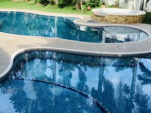 A swimming pool with a curved design, surrounded by a stone deck and a grassy area with trees. - Bella's Private Condominium (Dumaguete)