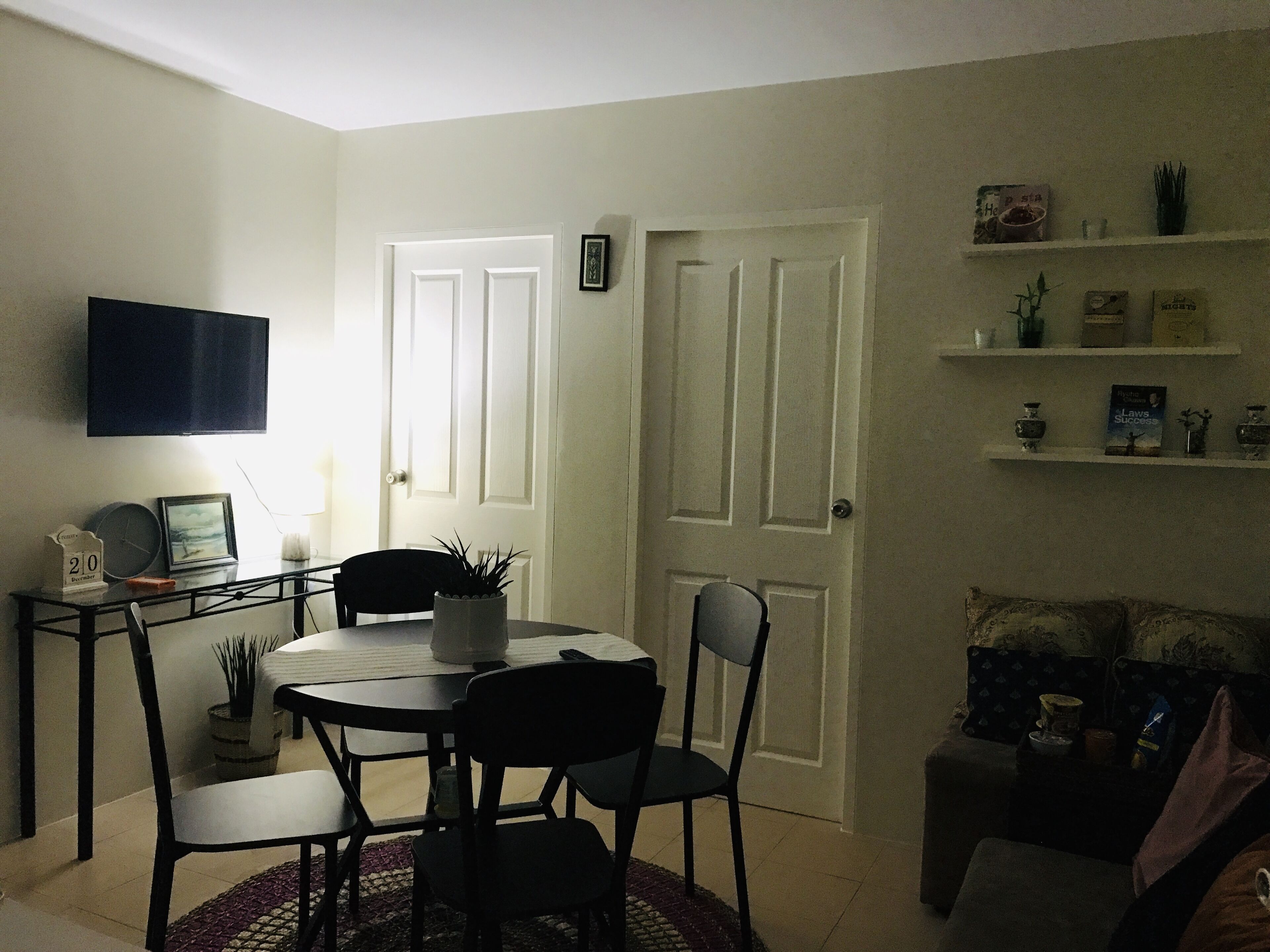 A dining area with a round table, chairs, a potted plant, and a television on the wall.